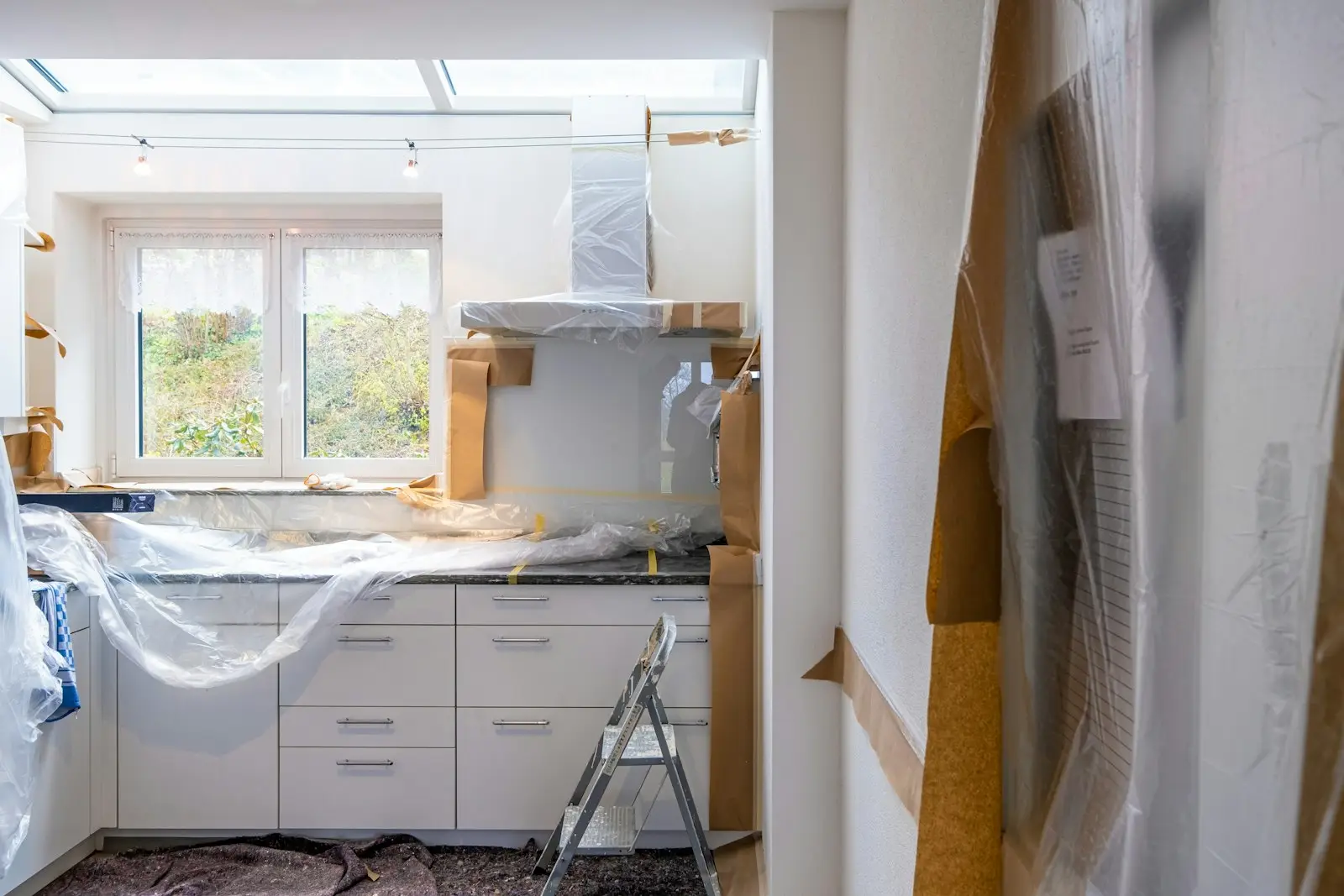Cocina en remodelación con gabinetes blancos protegidos con plástico y papel